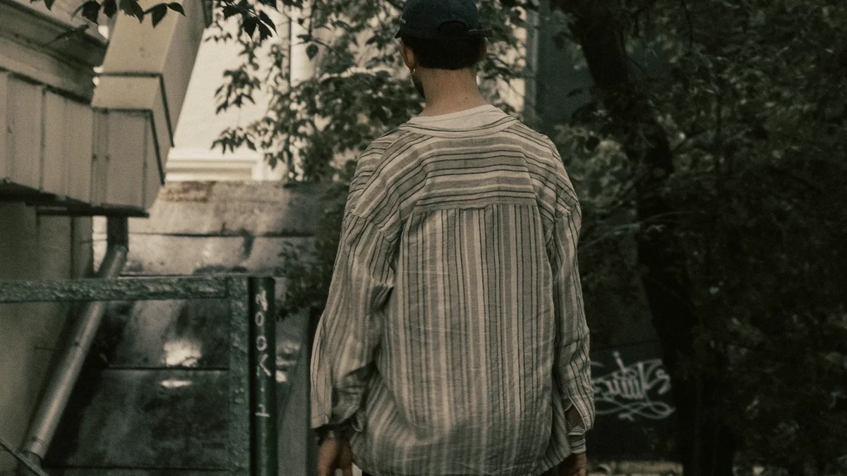 Mann mit Cap geht von der Kamera weg einen schattigen Weg zwischen Bäumen entlang