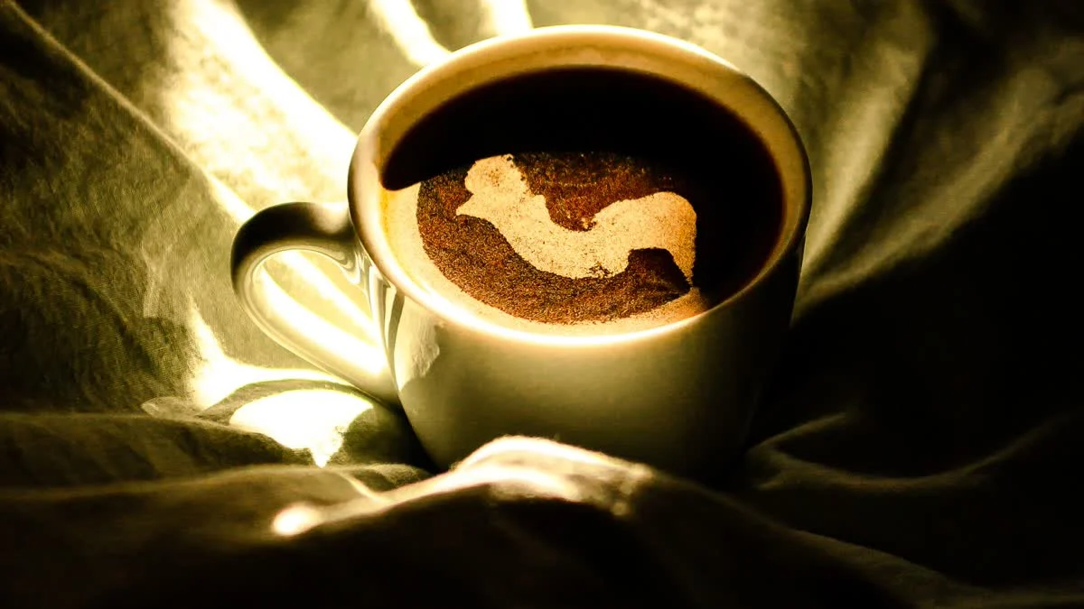 Kaffeetasse auf zerknitterter Bettwäsche im warmen Morgenlicht