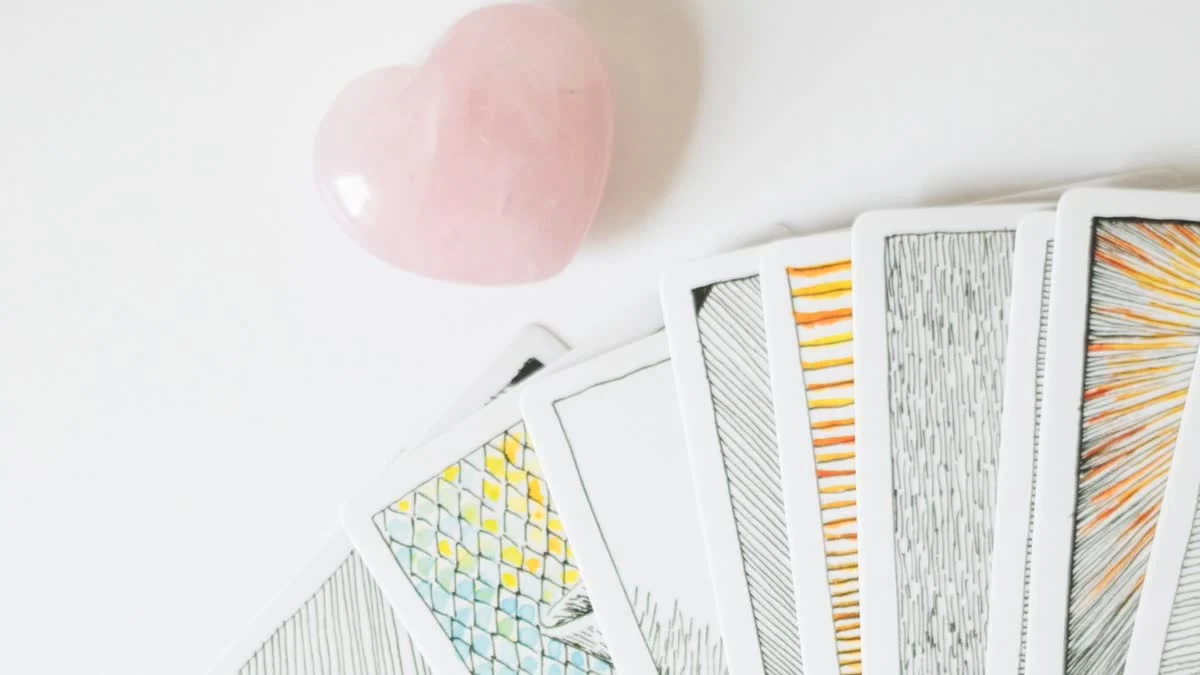 Aufgefächerte Tarotkarten neben einem herzförmigen Rosenquarz auf hellem Untergrund