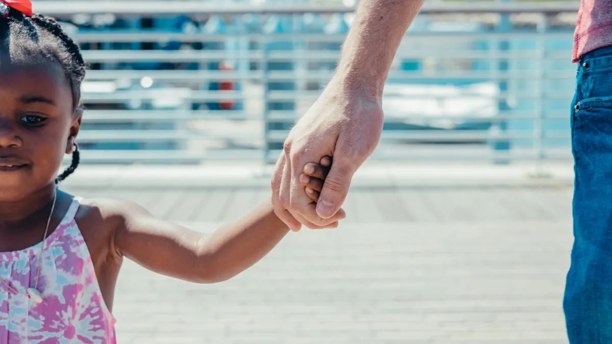 Kind hält beim Spaziergang im Freien die Hand eines Erwachsenen