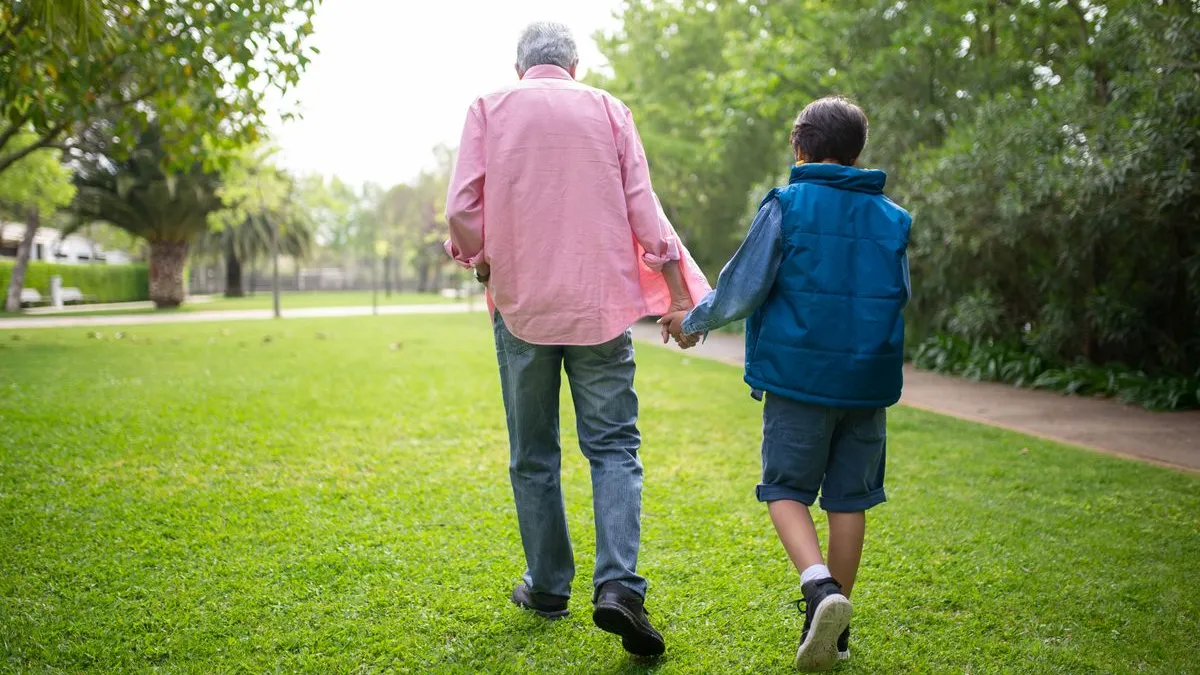 Großvater und Enkel gehen Hand in Hand über eine Wiese im Park