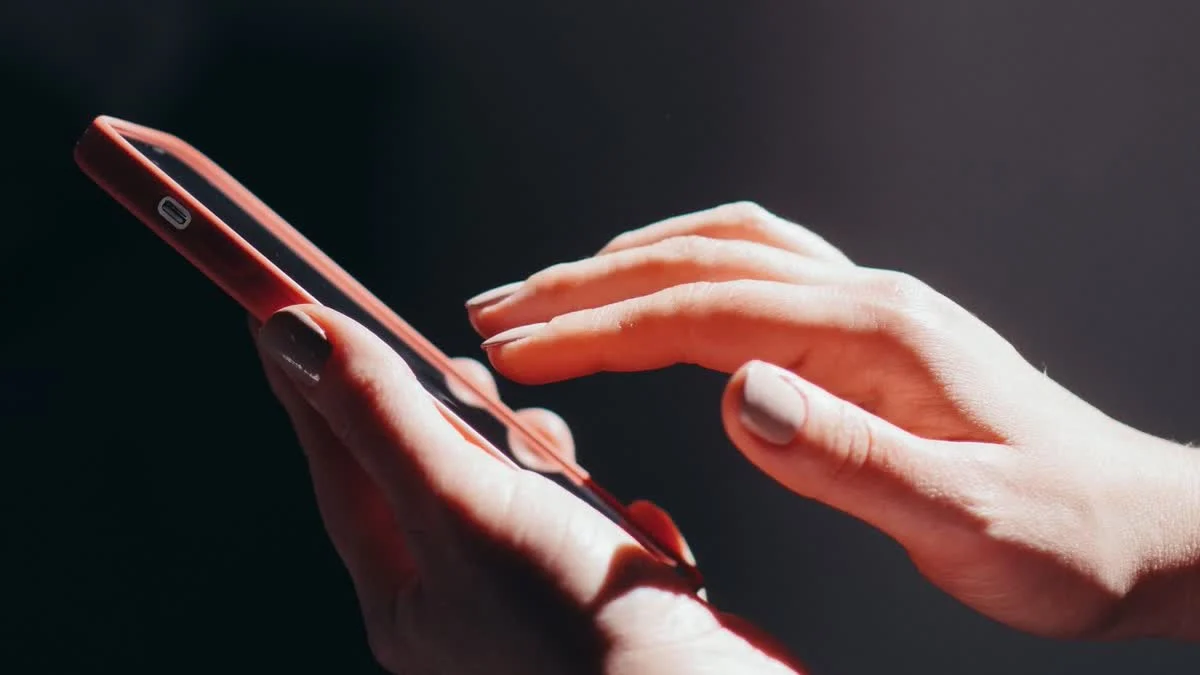 Zwei Hände halten ein Smartphone in warmem Licht vor dunklem Hintergrund