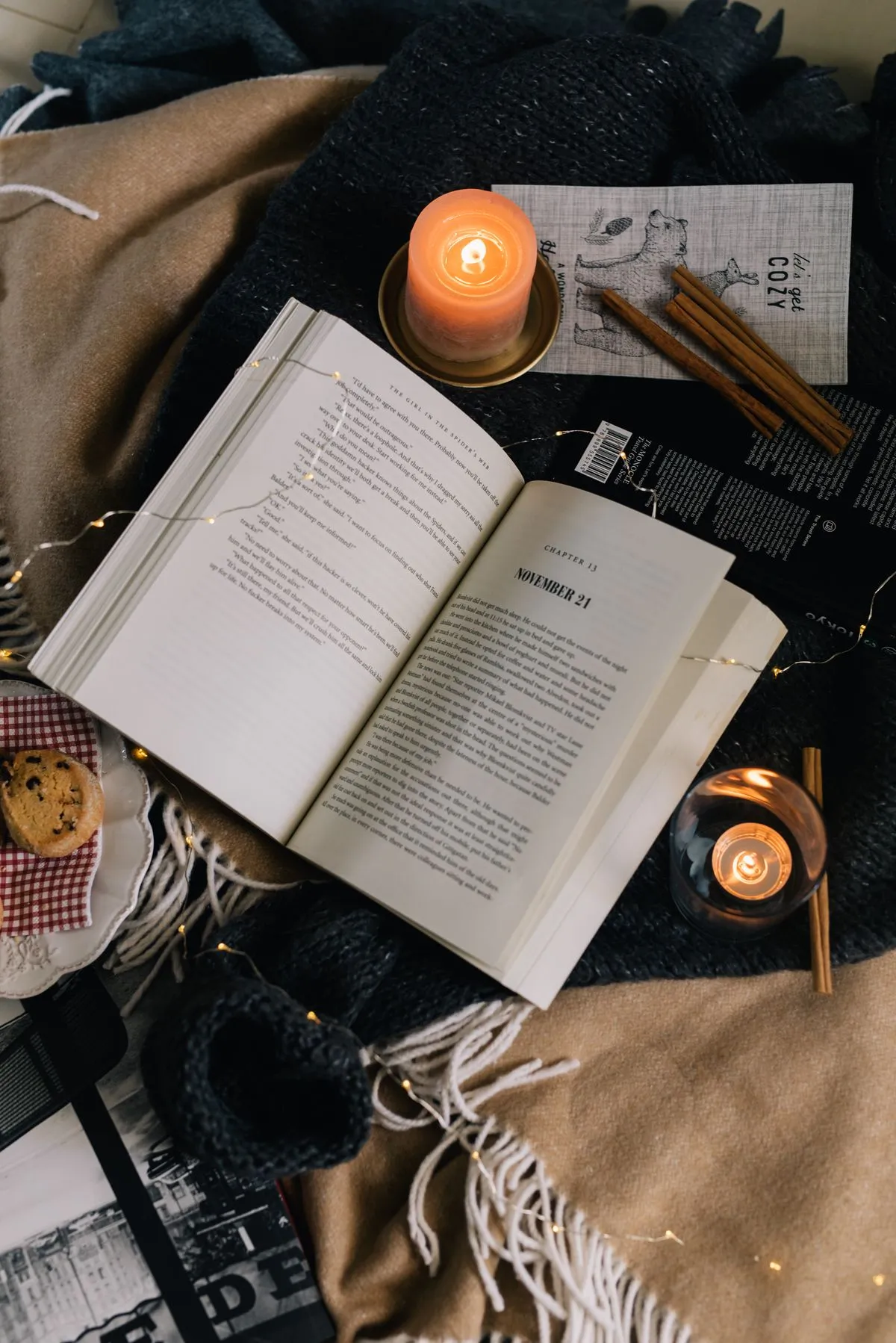 Aufgeschlagenes Buch mit brennenden Kerzen und einer kuscheligen Decke am Abend