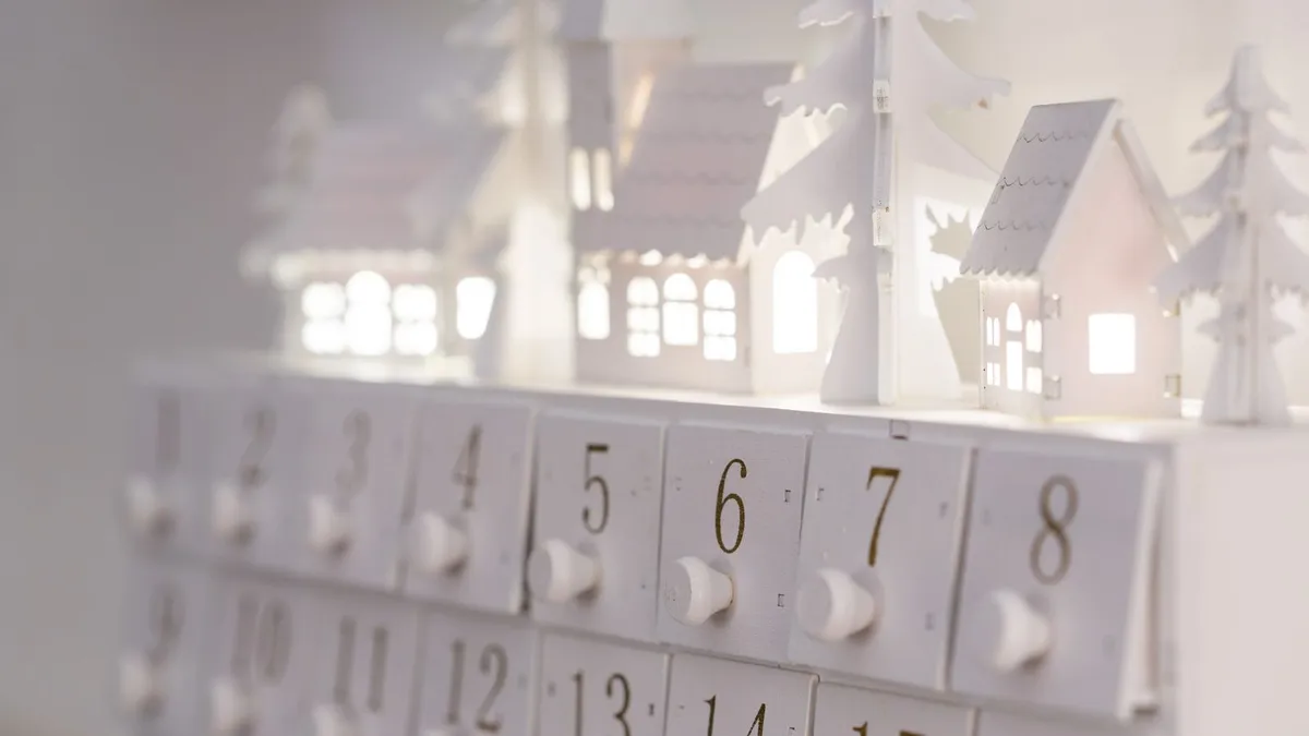 Weißer Adventskalender mit nummerierten Türchen und beleuchteten Holzhäuschen