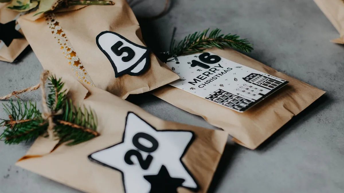 Adventskalender aus Papiertüten mit Zahlen, Sternanhängern und Tannenzweigen auf grauem Untergrund