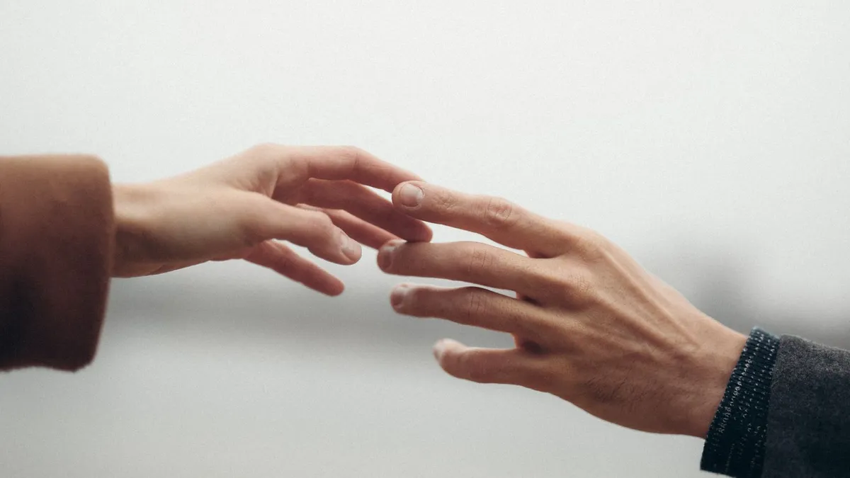 Zwei Hände strecken sich einander entgegen, die Fingerspitzen berühren sich fast
