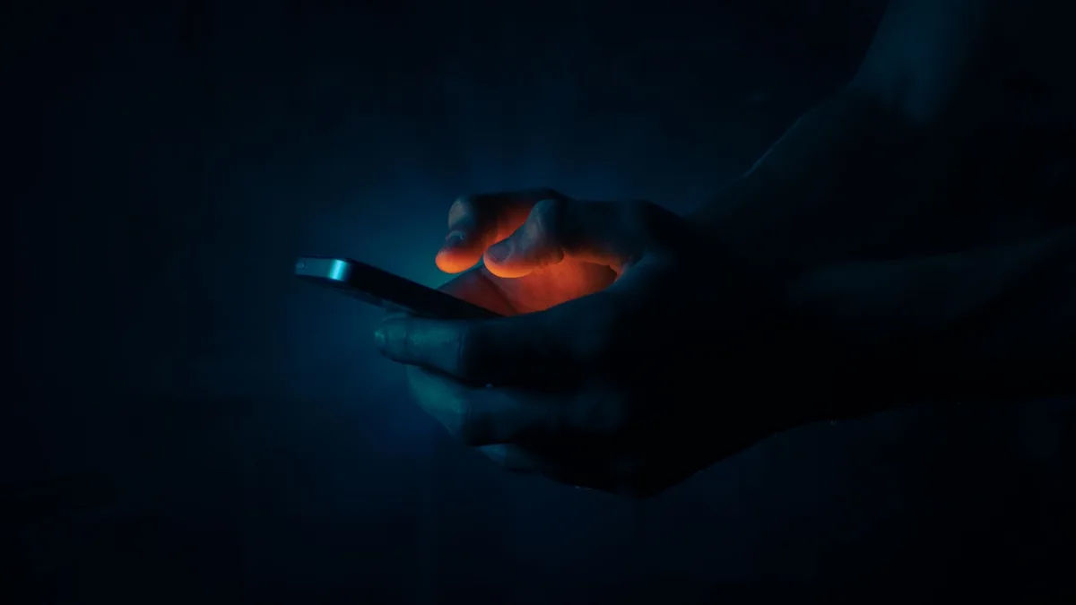Hände halten ein leuchtendes Smartphone im Dunkeln