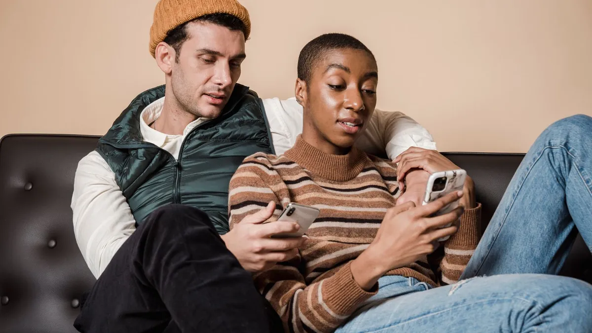 Ein Paar sitzt auf einem Ledersofa, beide schauen jeweils auf ihr eigenes Smartphone