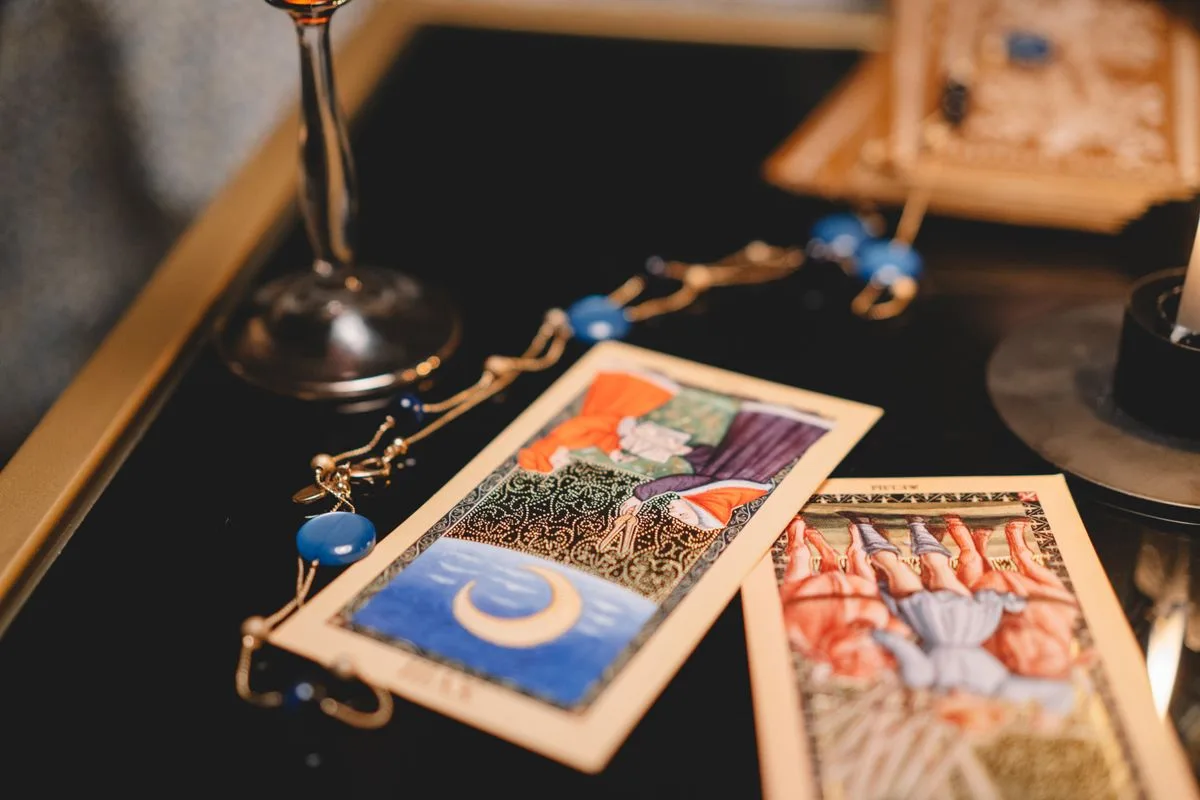 Aufgeschlagenes Horoskop-Magazin mit Sternzeichen-Symbolen neben einer Kaffeetasse und Tarotkarten auf einem hellen Holztisch