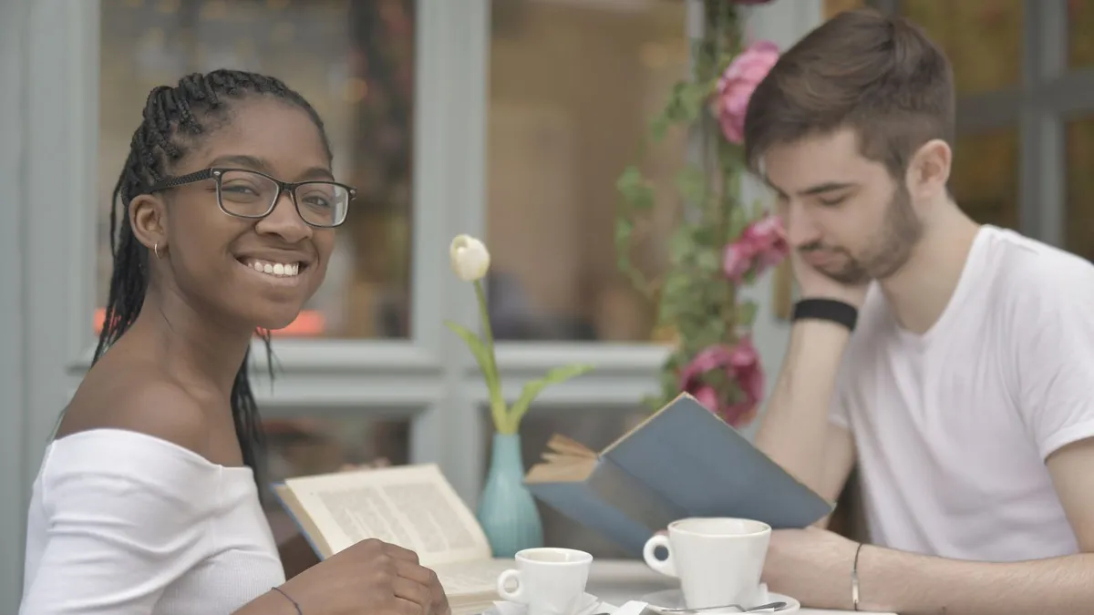 Lächelnde Frau und lesender Mann sitzen mit Kaffee an einem Tisch im Café