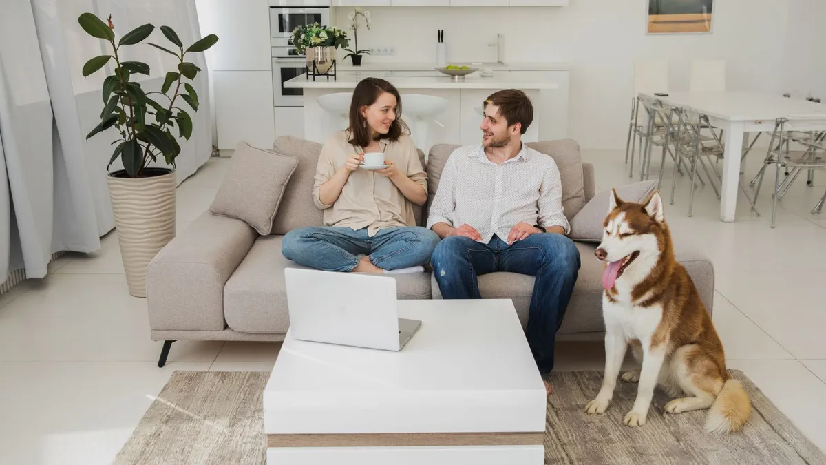 Paar sitzt mit Tee auf einem Sofa, daneben sitzt ein Husky auf dem Teppich