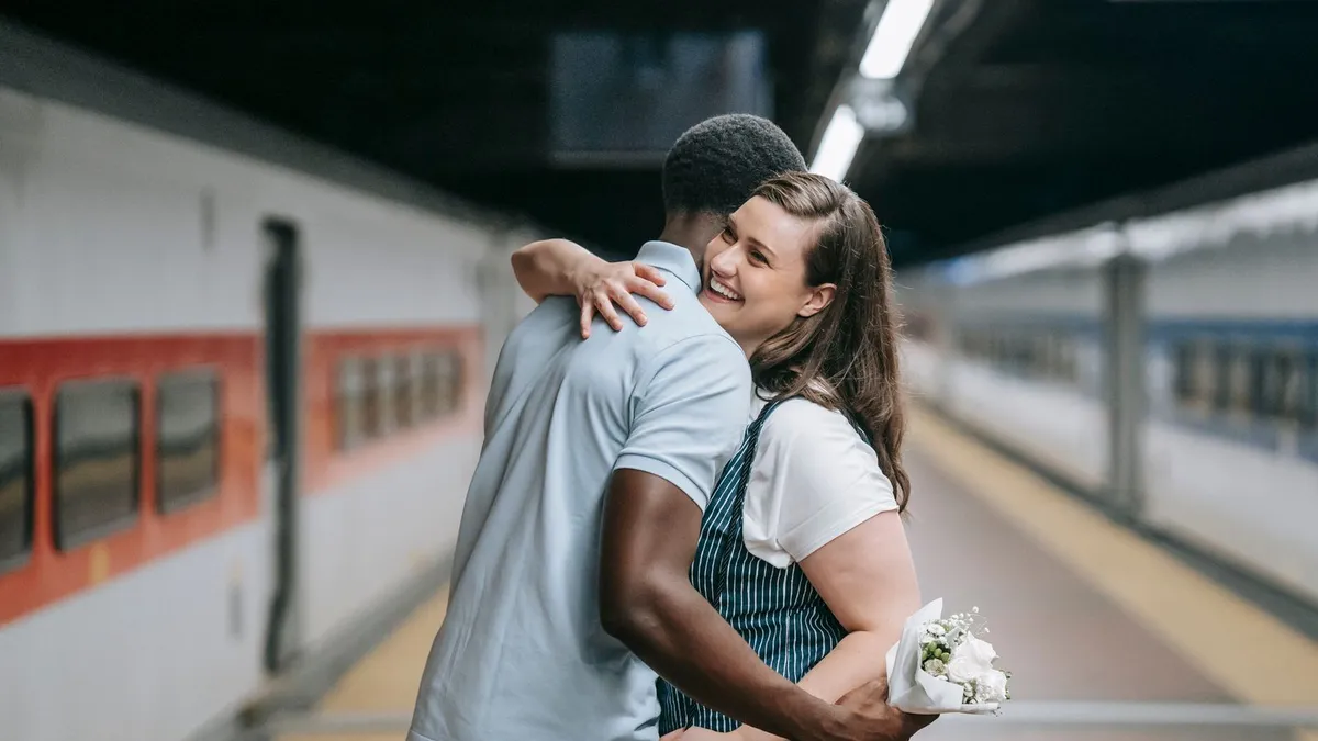 Wiedersehen auf dem Bahnsteig: Eine lachende Frau mit Blumenstrauß umarmt einen Mann