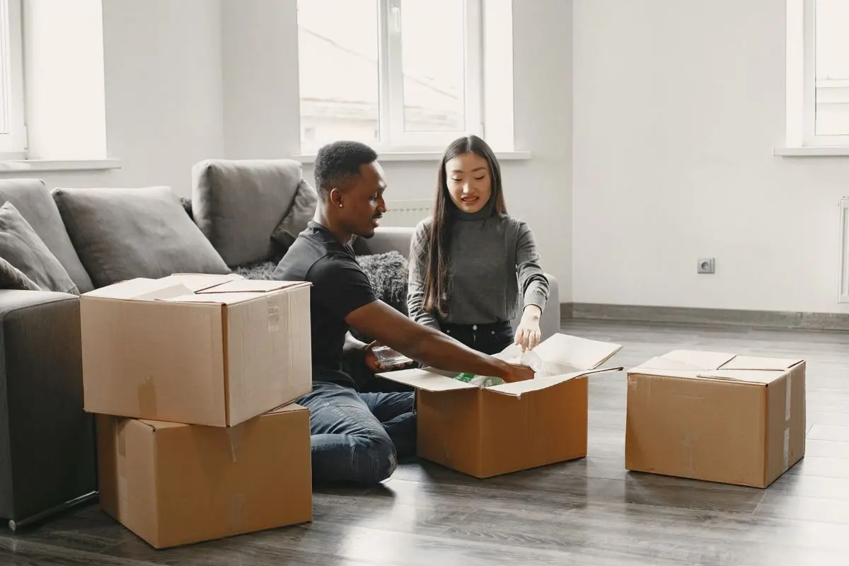 Paar packt gemeinsam Umzugskartons in der neuen Wohnung aus