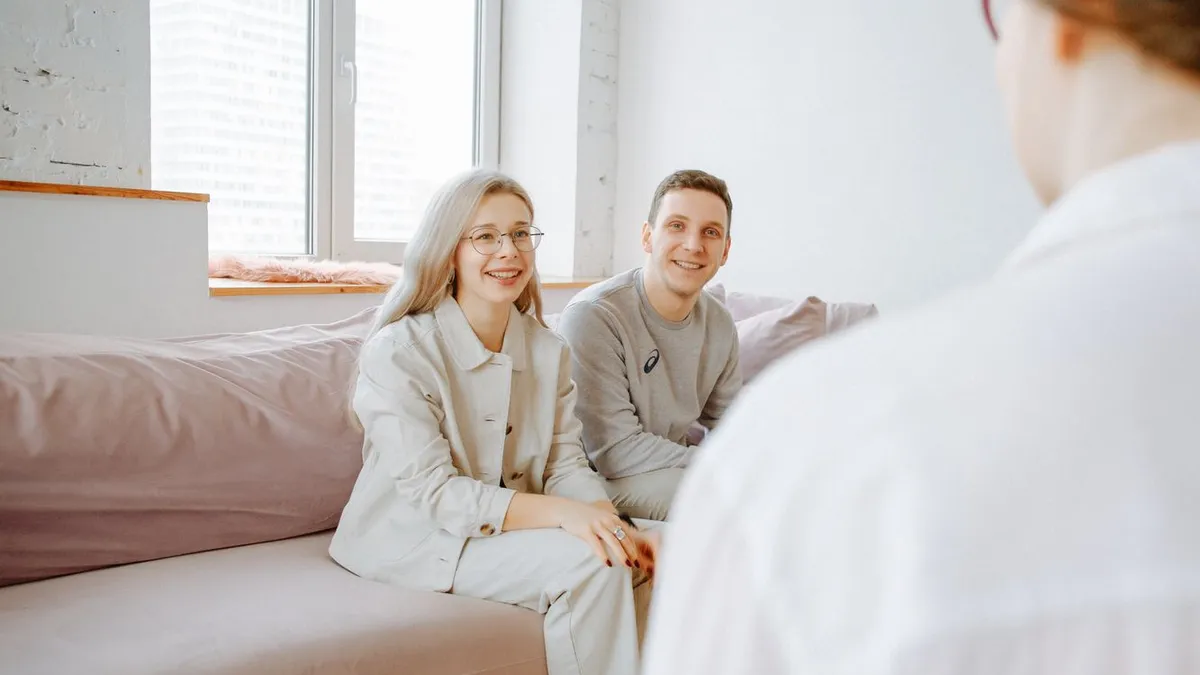 Lächelndes Paar sitzt auf einem Sofa, im Vordergrund ist eine Person von hinten zu sehen