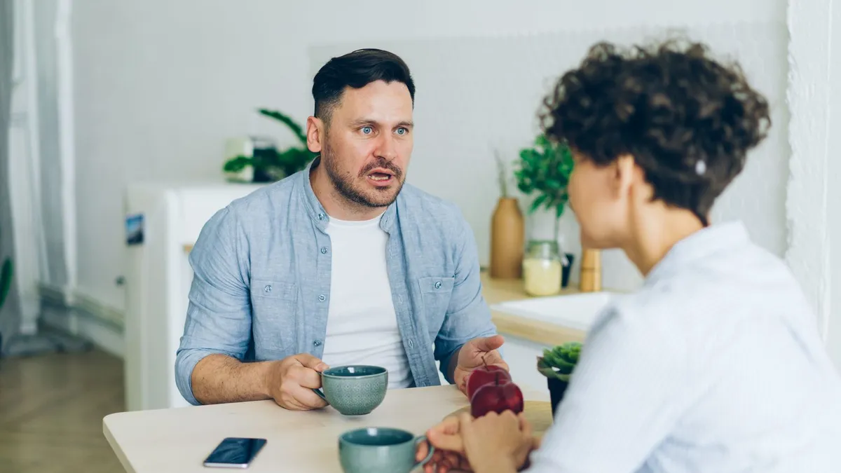 Mann und Frau führen am Küchentisch bei Kaffee ein ernstes Gespräch