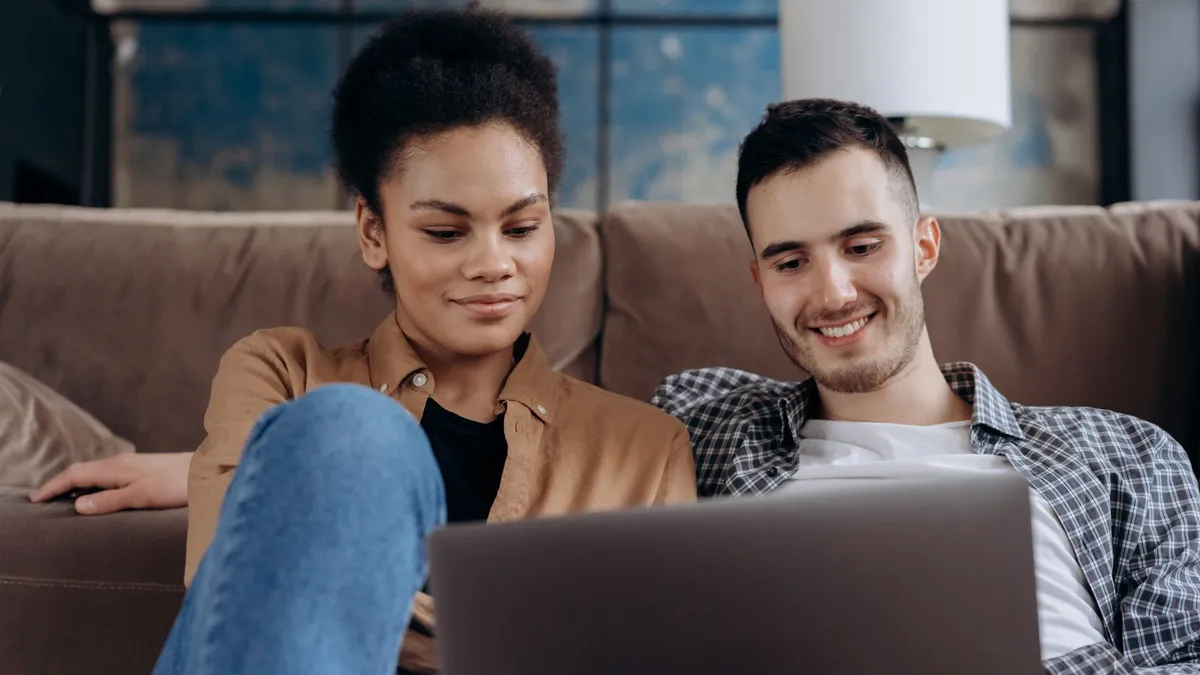 Paar sitzt lächelnd auf dem Sofa und schaut gemeinsam auf einen Laptop