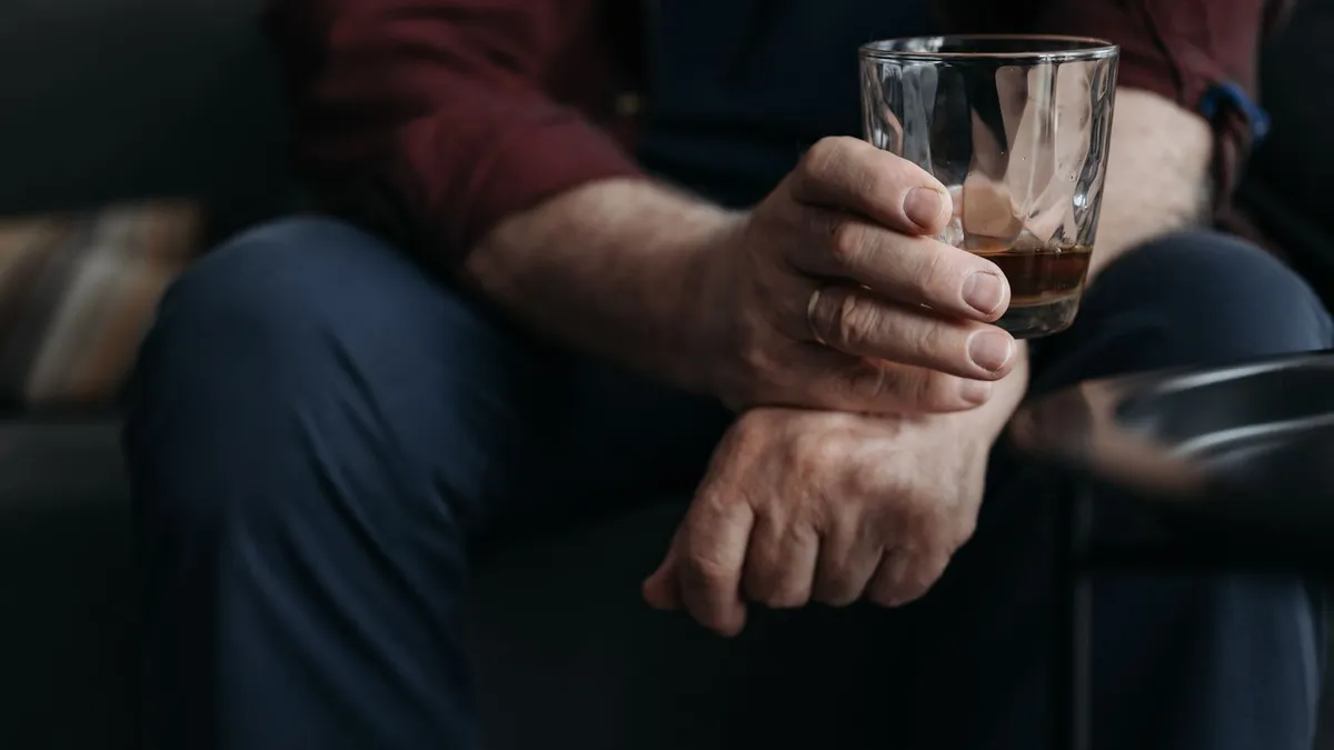 Hand mit Ring hält ein Glas mit einem Rest eines braunen Getränks