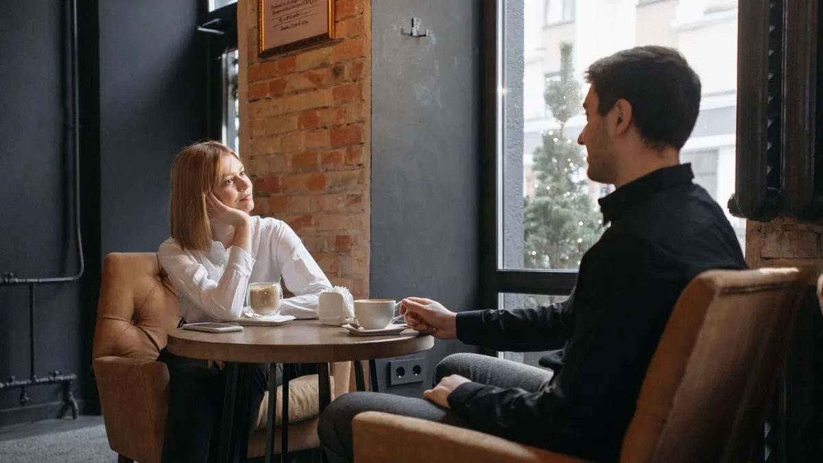 Frau und Mann sitzen im Café an einem kleinen Tisch, sie blickt gedankenverloren zur Seite