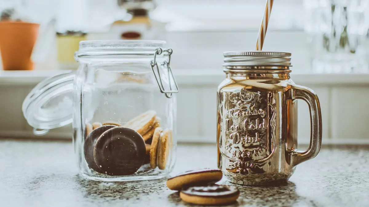 Glas mit Schokoladenkeksen auf einer Küchenarbeitsplatte neben einem Henkelbecher mit Strohhalm