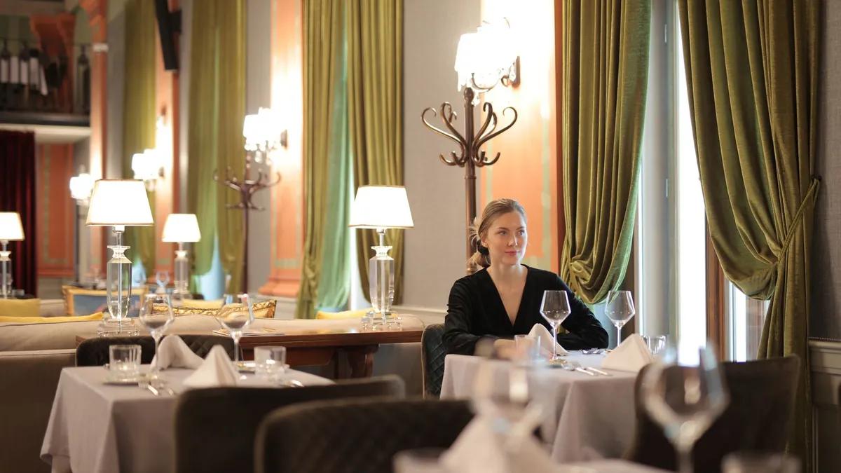 Frau sitzt allein an einem festlich gedeckten Tisch in einem eleganten Restaurant und wartet