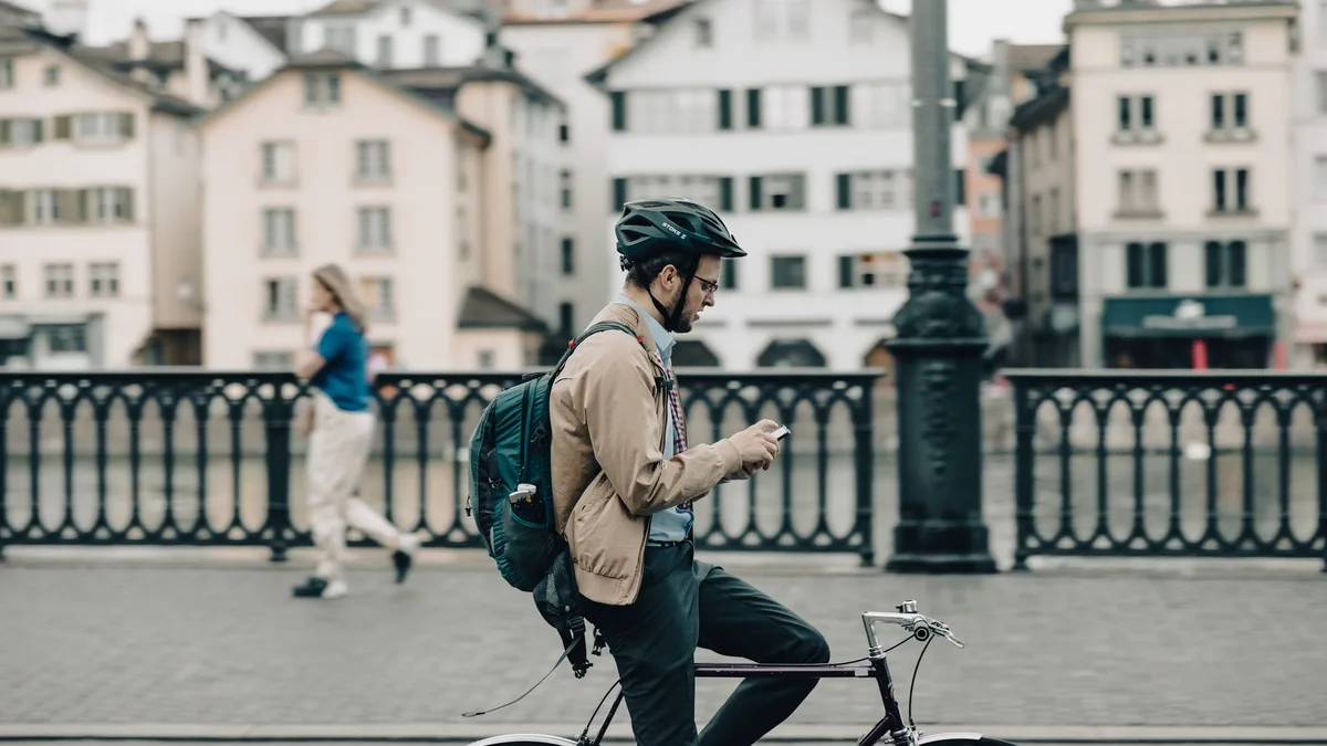 Radfahrer mit Helm hält auf einer Brücke in der Altstadt an und schaut auf sein Smartphone