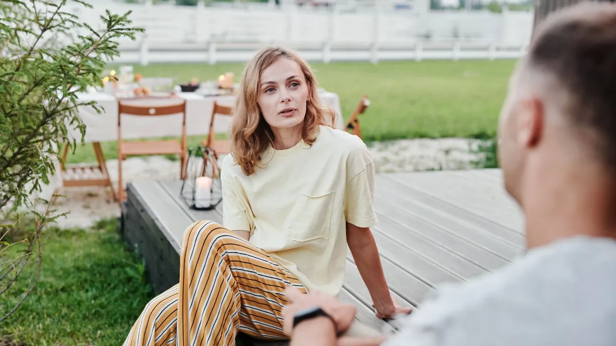 Frau und Mann sitzen sich auf einer Holzterrasse im Garten gegenüber und führen ein ernstes Gespräch