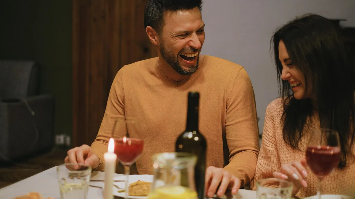 Mann und Frau lachen herzlich bei einem Abendessen mit Kerze und Rotwein
