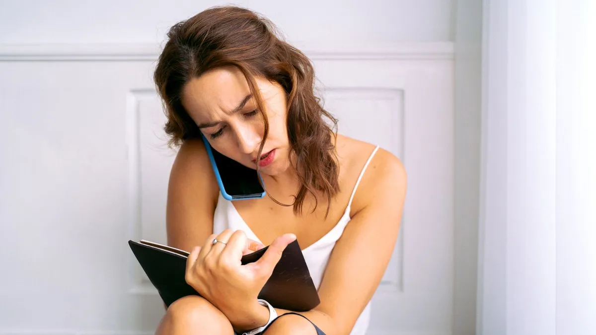 Frau klemmt das Handy zwischen Schulter und Ohr und schaut angestrengt in ein Notizbuch