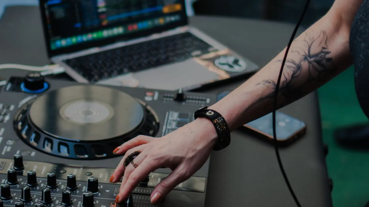 Hand an einem DJ-Controller, im Hintergrund ein Laptop mit Musiksoftware
