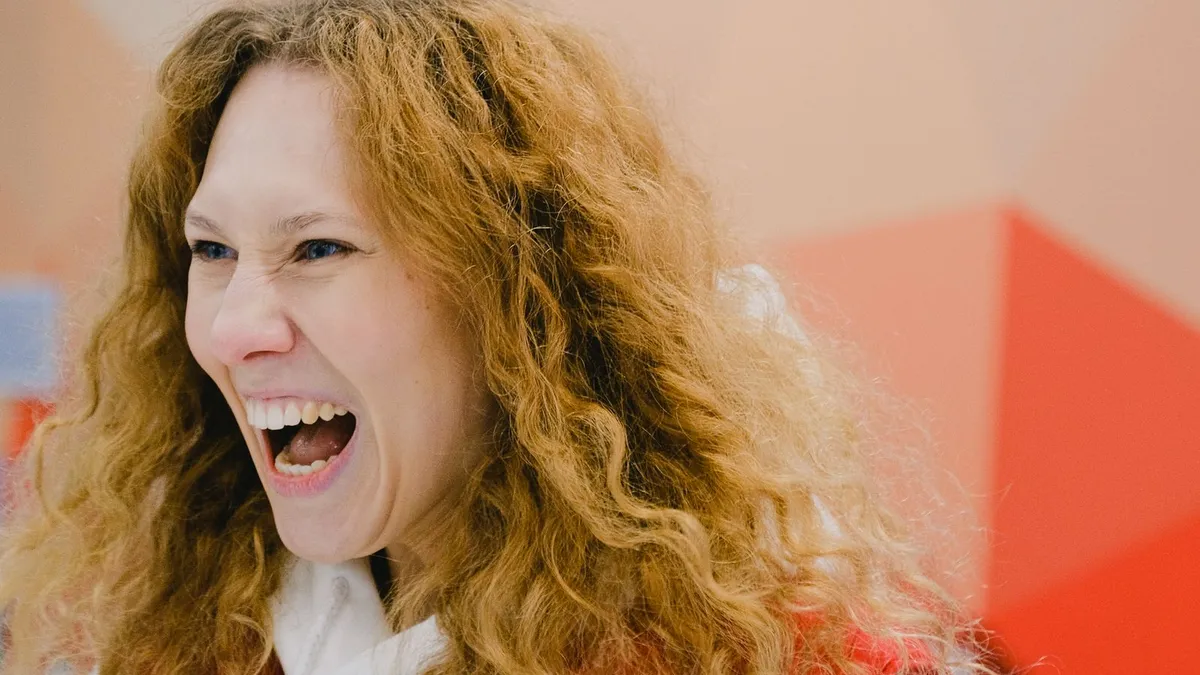 Frau mit roten Locken lacht herzhaft vor buntem Hintergrund