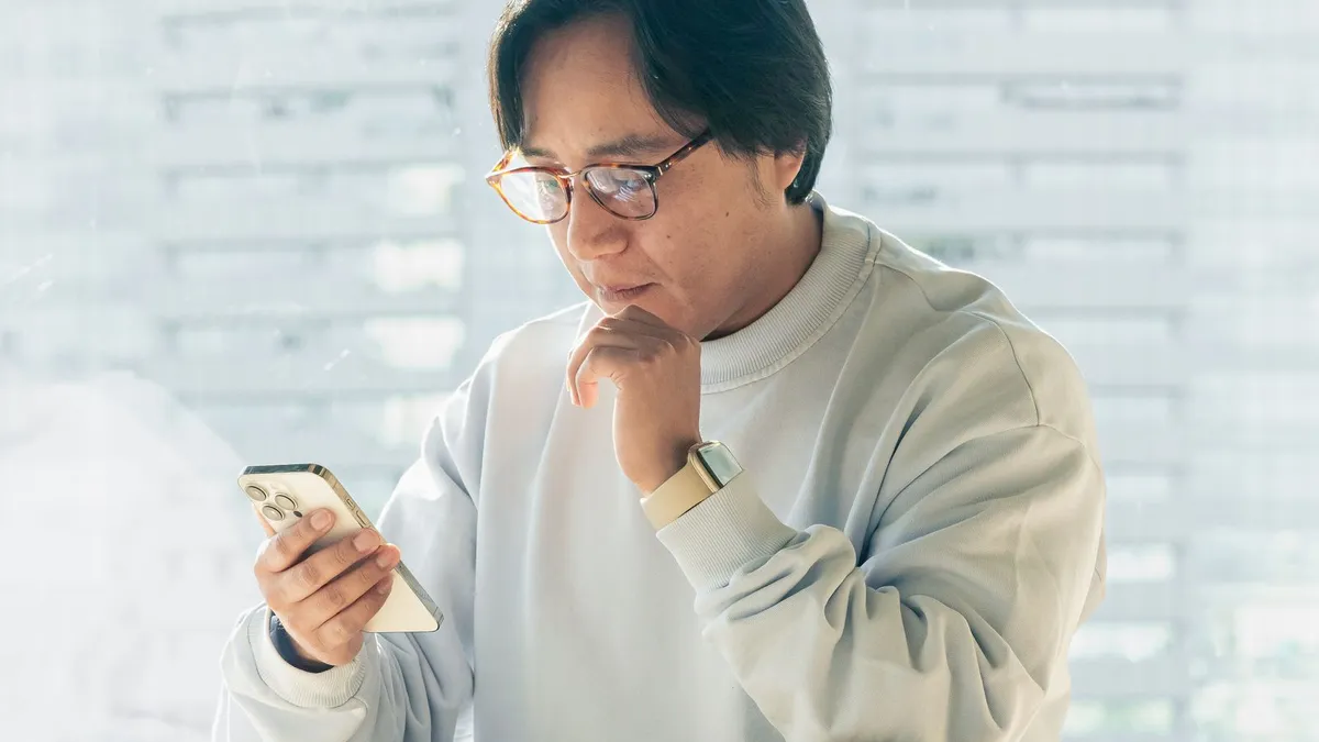 Mann mit Brille schaut nachdenklich auf sein Smartphone und stützt das Kinn auf die Hand