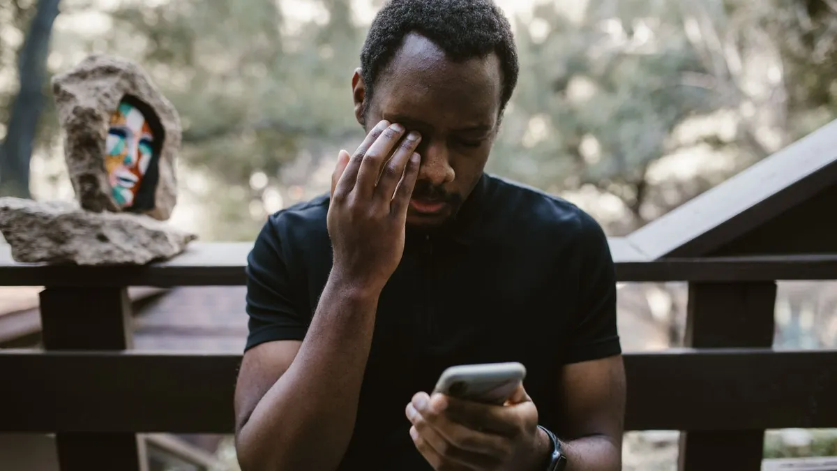 Mann fasst sich an die Augen und liest bedrückt eine Nachricht auf seinem Smartphone