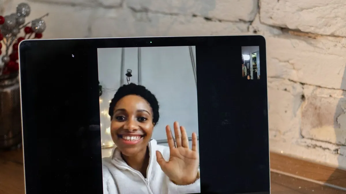 Lächelnde Frau winkt in einem Videoanruf vom Laptopbildschirm aus in die Kamera