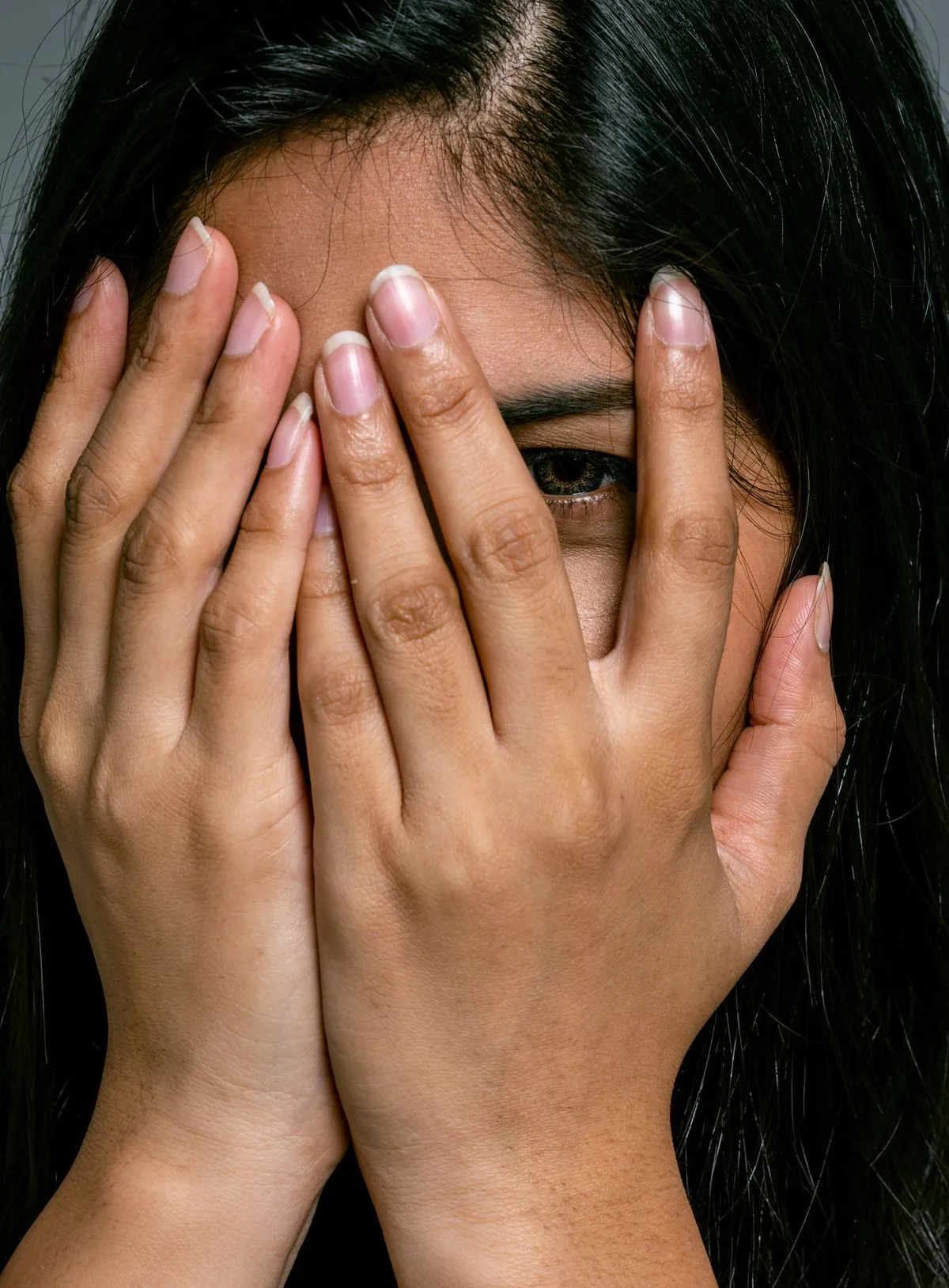 Frau verdeckt ihr Gesicht mit beiden Händen und lugt mit einem Auge durch die Finger