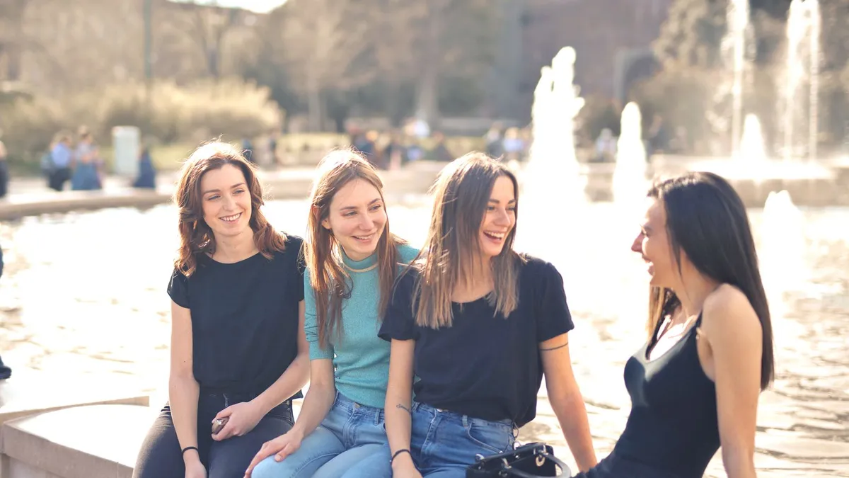 Vier junge Frauen sitzen lachend und plaudernd an einem Springbrunnen