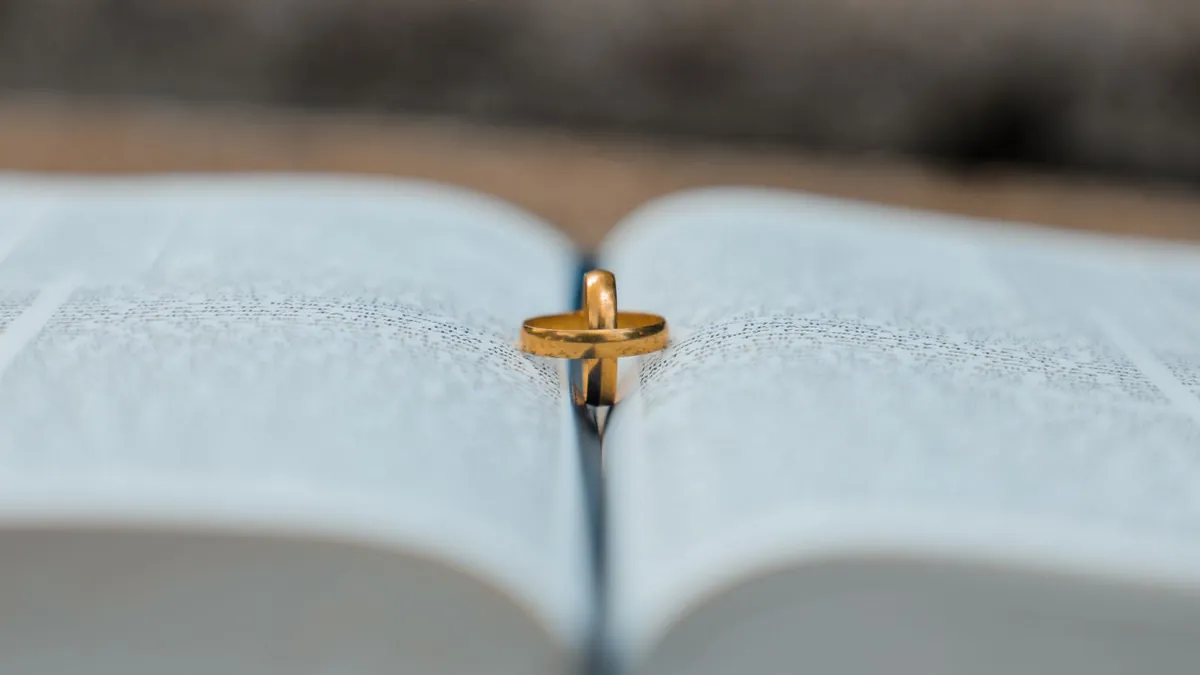 Zwei goldene Eheringe stehen ineinander auf einem aufgeschlagenen Buch