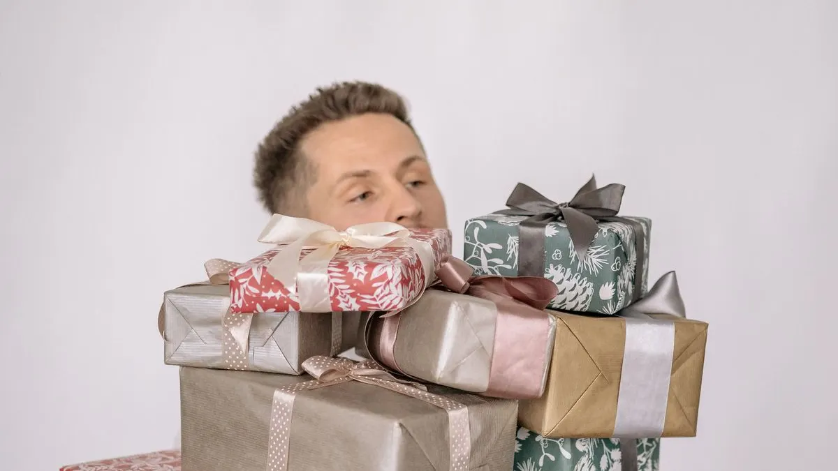 Mann schaut hinter einem hohen Stapel verpackter Geschenke hervor
