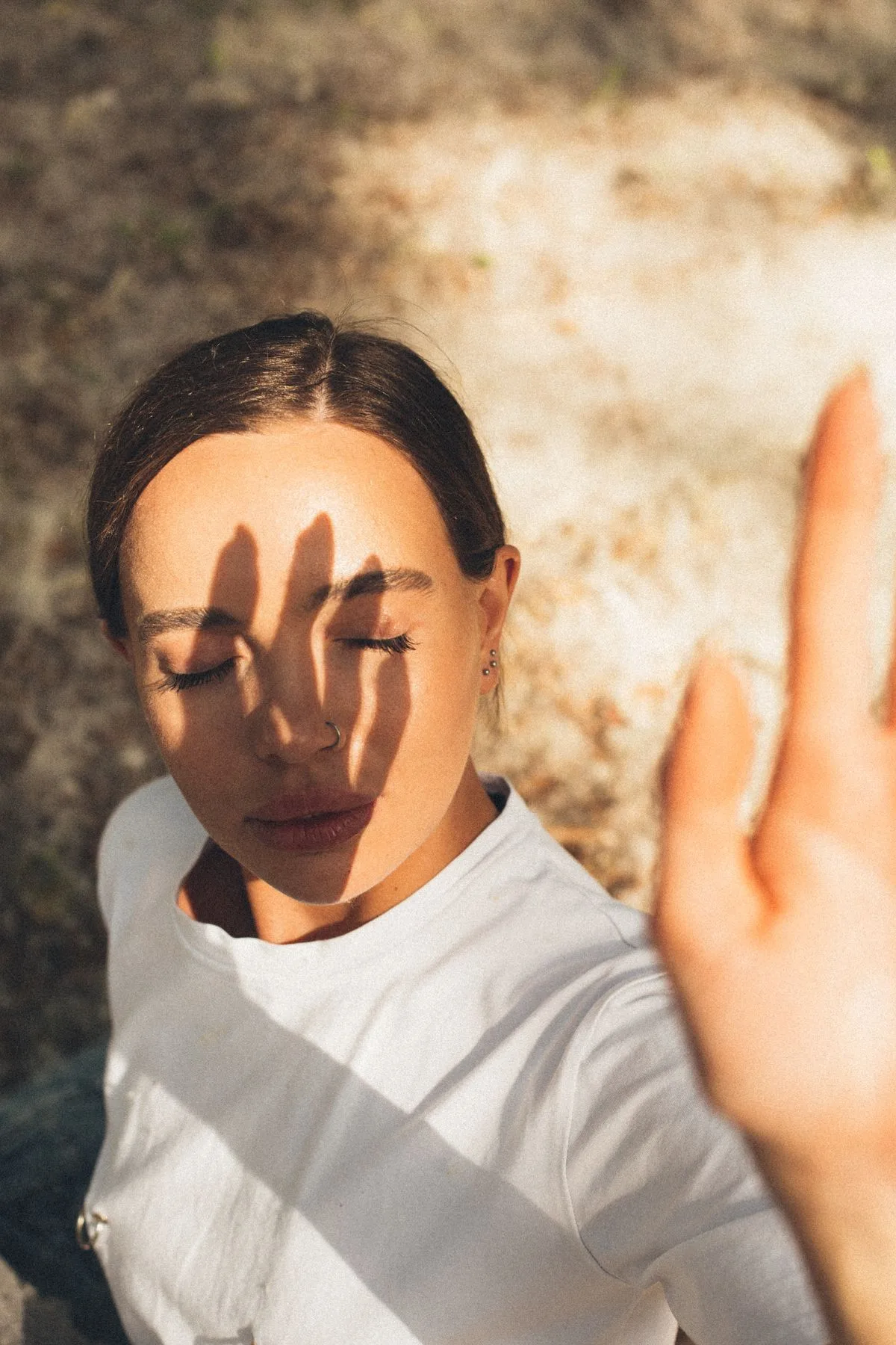 Frau mit geschlossenen Augen im warmen Sonnenlicht, ein Schattenmuster fällt über ihr Gesicht