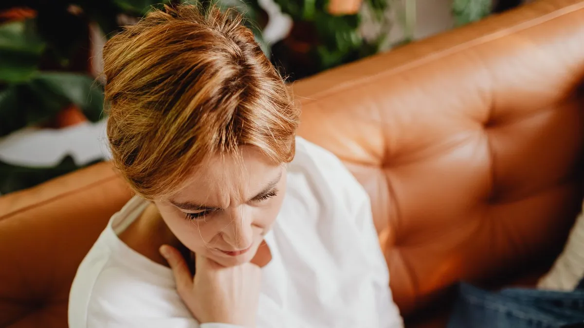 Nachdenkliche Frau mit rotblondem Haar sitzt auf einem Ledersofa, die Hand am Kinn