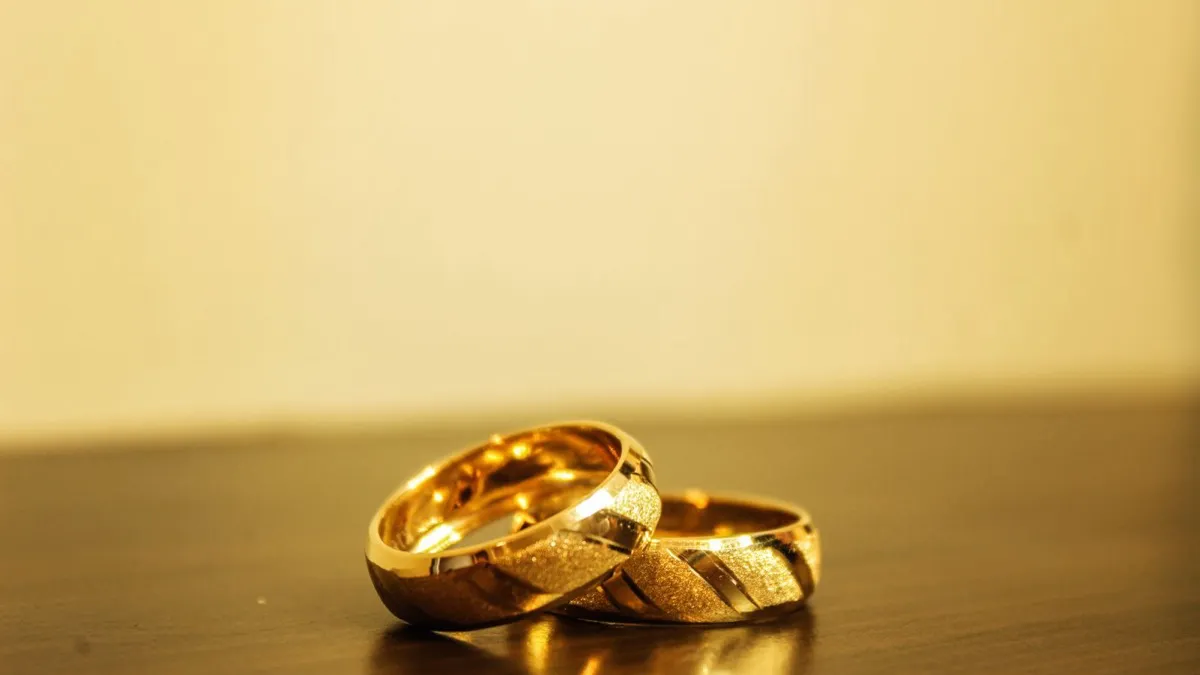 Zwei goldene Eheringe liegen ineinander auf einer dunklen Holzfläche in warmem Licht