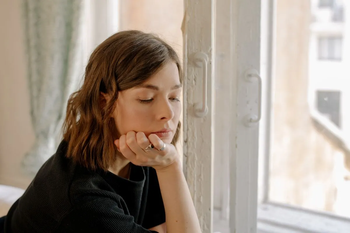 Nachdenkliche Person am Fenster, in Gedanken versunken — Symbolbild Grübeln