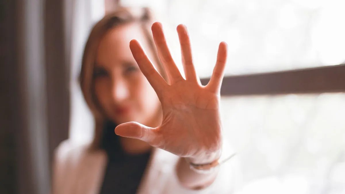 Frau hält abwehrend die Hand mit gespreizten Fingern in die Kamera, ihr Gesicht ist unscharf