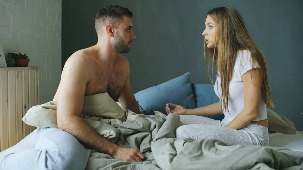 Paar sitzt einander zugewandt auf dem Bett in einem ruhigen Gespräch