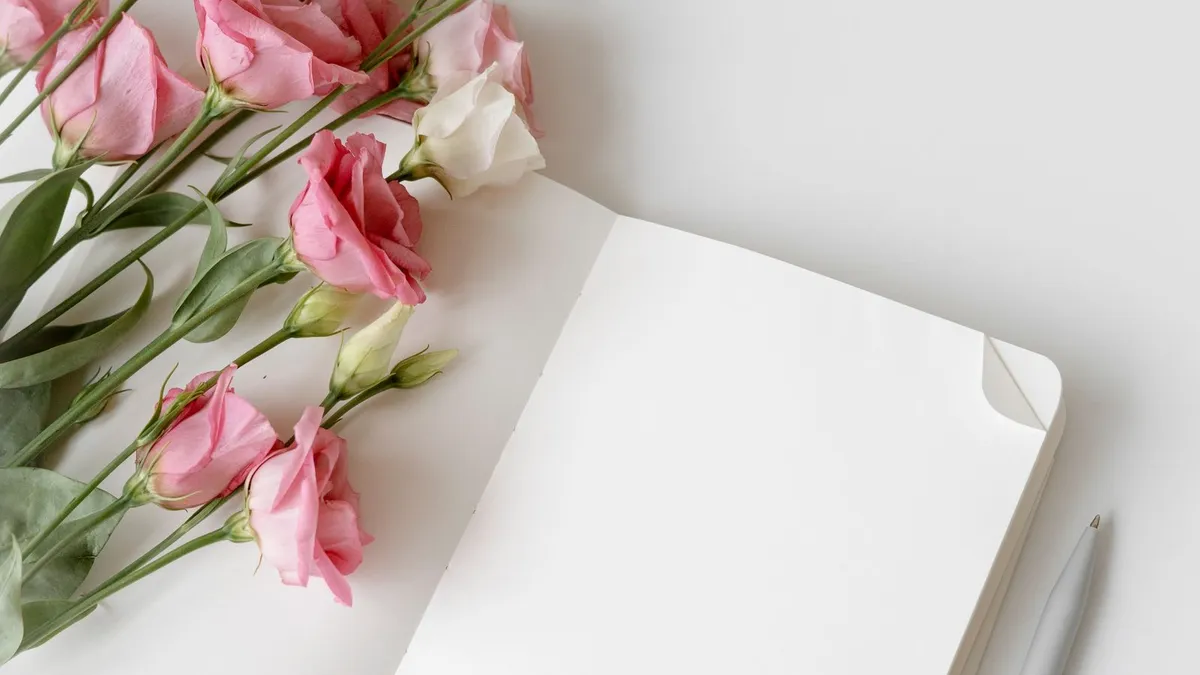 Aufgeschlagenes leeres Notizbuch mit Stift neben einem Strauß rosa Eustoma-Blüten