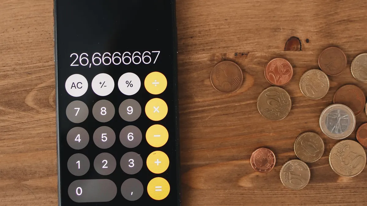 Smartphone mit Taschenrechner-App neben Euro-Münzen auf einem Holztisch