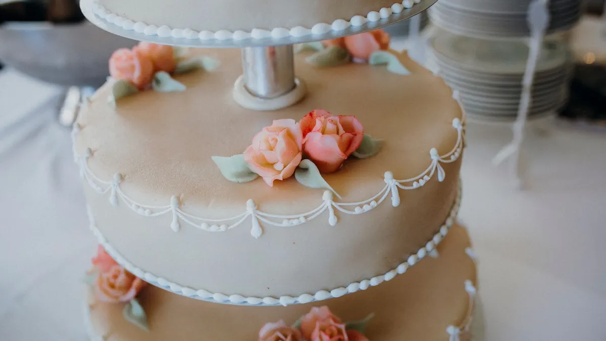 Mehrstöckige Hochzeitstorte mit hellem Überzug, weißen Zuckerperlen und rosa Zuckerrosen