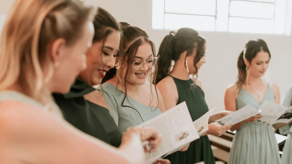 Mehrere Frauen in grünen Kleidern lesen lächelnd in gedruckten Heften