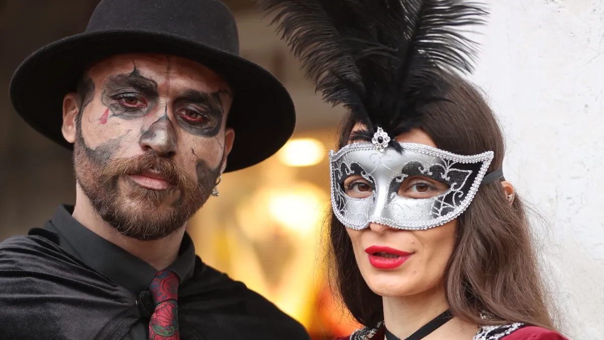 Paar bei einer Maskenparty: Mann mit Hut und geschminktem Gesicht, Frau mit silberner venezianischer Maske