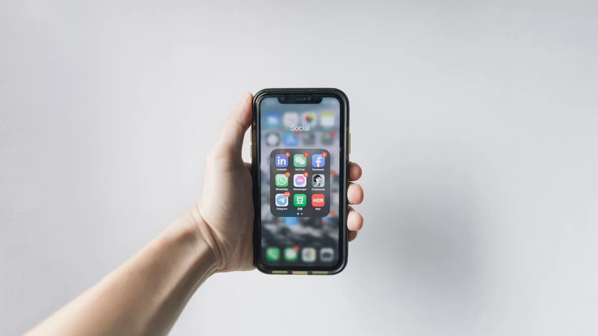 Hand hält ein Smartphone mit App-Übersicht vor hellem Hintergrund