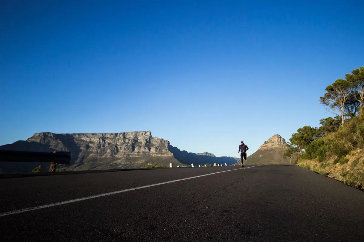 Läufer joggt frühmorgens auf einer Bergstraße vor blauem Himmel